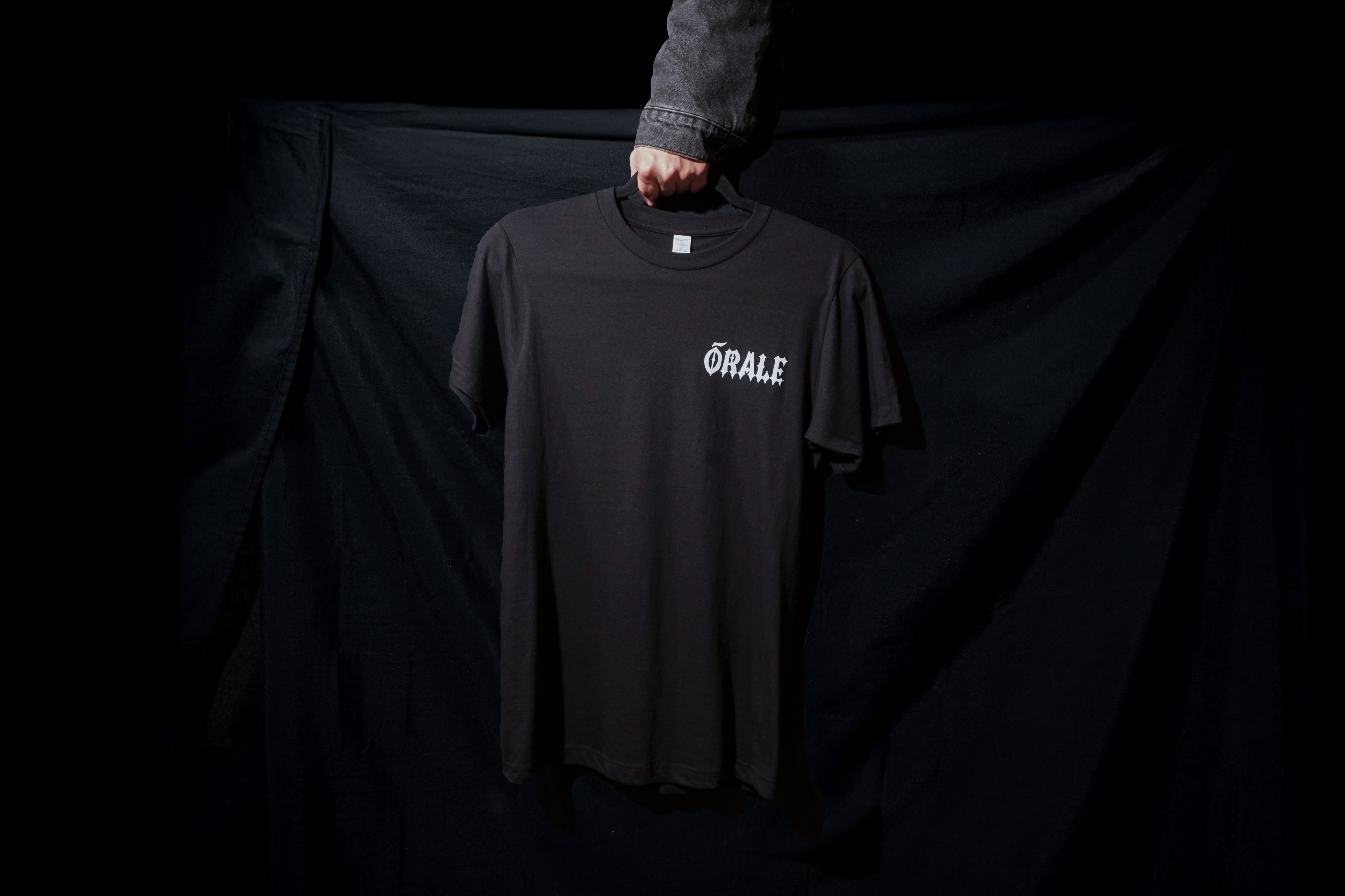 Black t-shirt with 'ORALE' logo held by a person against a black background